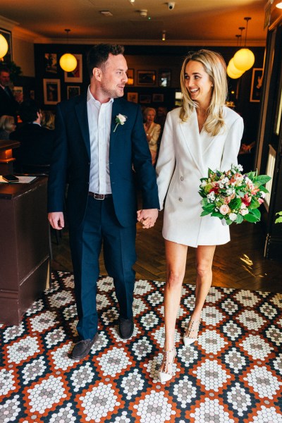 bride and groom stand inside wedding venue looking at each other holding hands and bouquet in hand