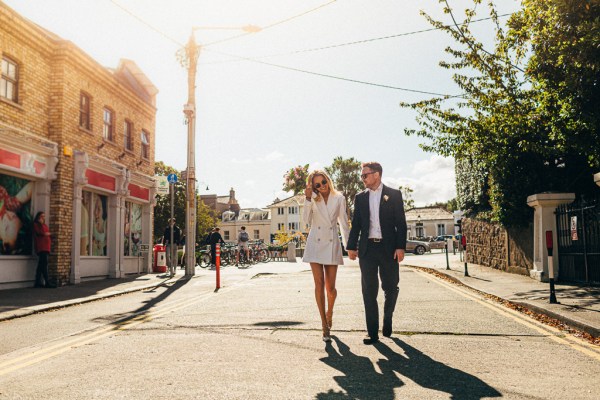 bride and groom walking along road/pathway holding hands in the sunshine