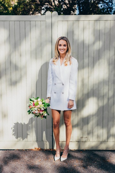 bride stands holding bouquet flowers in front of wall