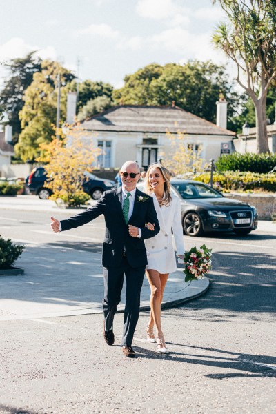 bride and groom walk on the road to stately wedding venue car in background