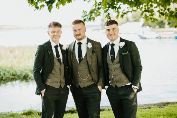 groom and groomsmen stand beside lake setting