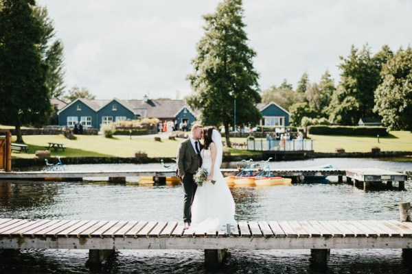 bride and groom kiss standing on boardwalk over lake