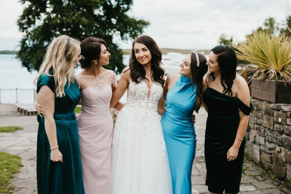 bride and female friends lake in background they walk in a row