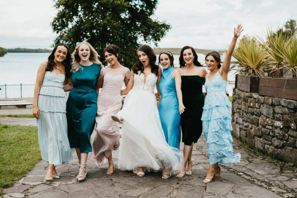 bride and female friends lake in background they walk in a row