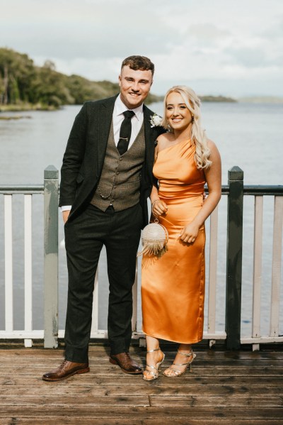 woman in orange dress with man on boardwalk overlooking lake