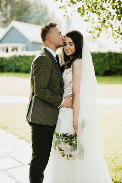 groom kisses bride on the forehead in garden setting