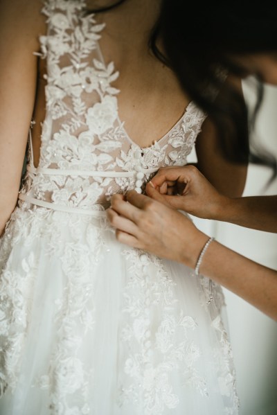 bridesmaid helps bride with back of dress