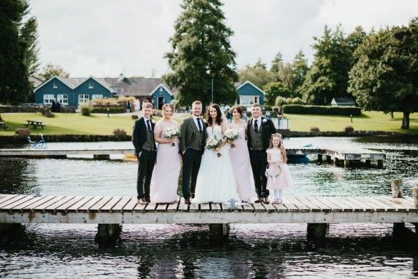 bride groom bridesmaid and groomsmen stand on boardwalk over lake