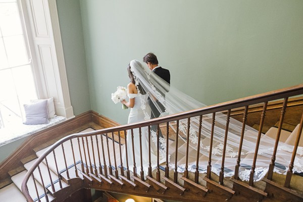 father and bride walk down the staircase as her veil follows