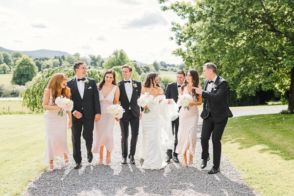 Bride groom groomsmen and bridesmaids walk along pathway to garden