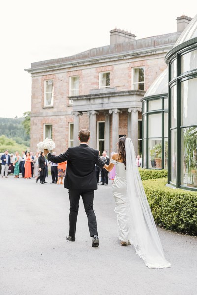 bride and groom from behind he holds her white bouquet in courtyard to wedding venue