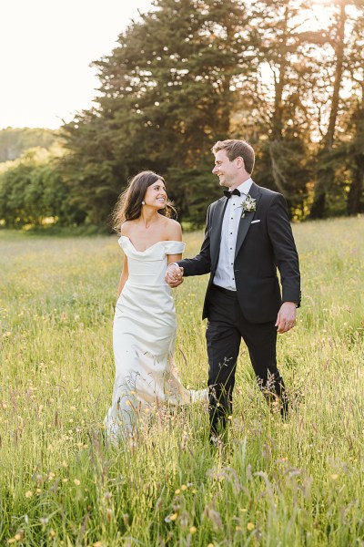 bride and groom walk on the grass as the sun sets in garden setting