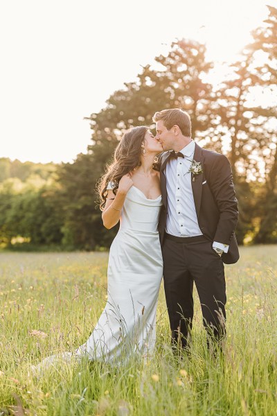 bride and groom kiss on the grass as the sun sets in garden setting