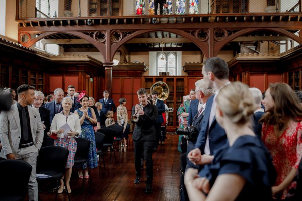 wide shot of wedding band playing trumpet saxophone and trombone down the aisle