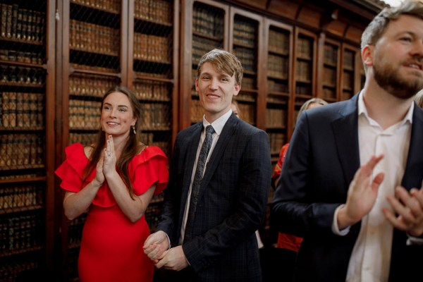 man in audience smiling beside woman wearing red dress clapping