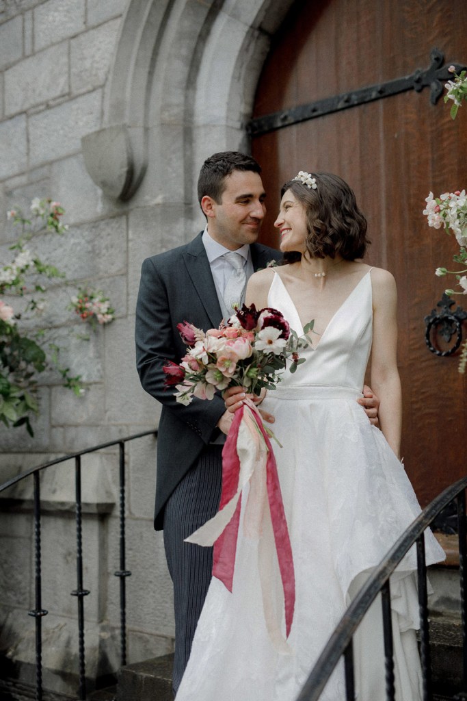 bride and groom standing on the steps to wedding church venue hugging