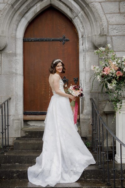 bride stands on her own in front of wedding venue church holding bouquet