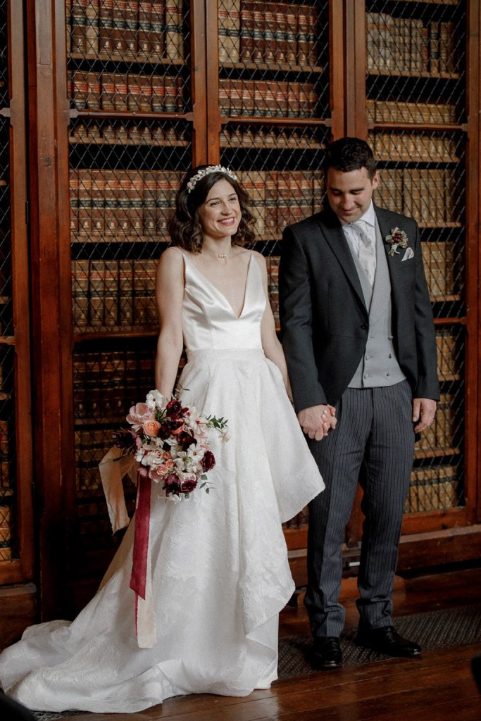 bookcase interior library setting bride and groom hand in hand standing straight