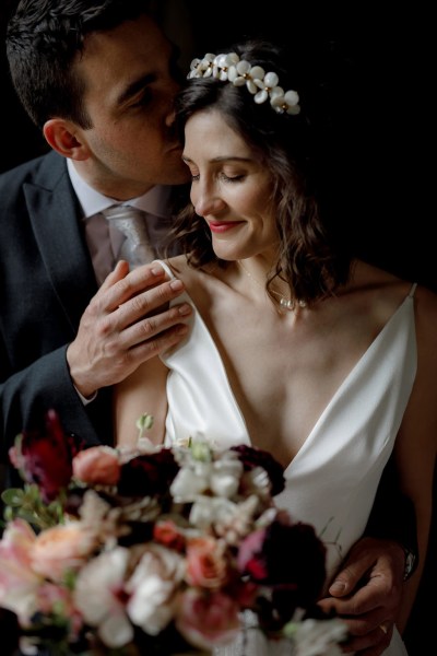 groom puts hand on brides shoulder she looks to the side and smiles