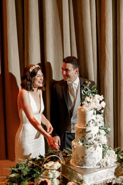 bride and groom cut the white wedding cake covered in flowers