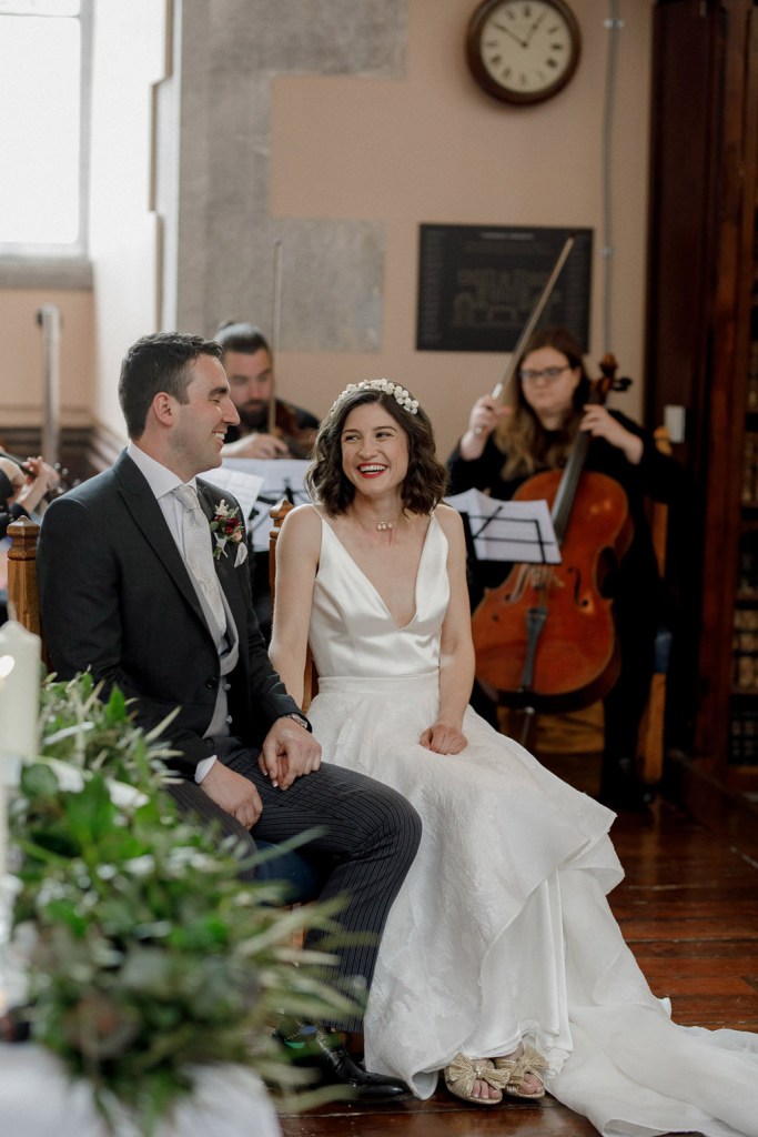 bride and groom sit happily in front of priest/celebrant during ceremony