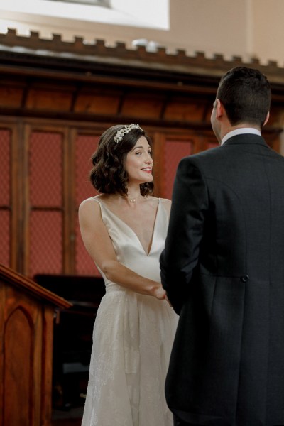 bride and groom smile hold hands at the alter