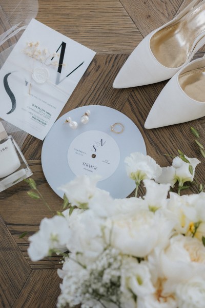 initials wedding band ring and jewelry white bridal heels shoes and perfume resting on bridal veil and blue plate