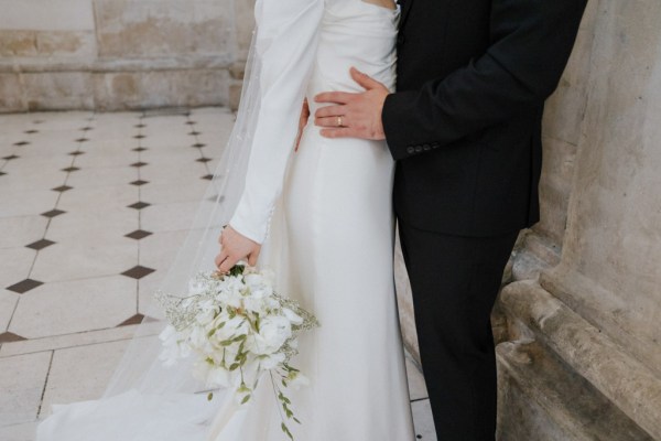 groom has his hands around brides waist and bouquet is in shot