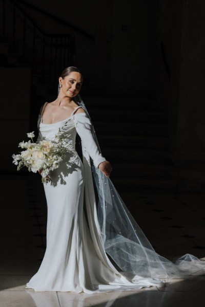 dark photo of bride showing off veil and dress holding bouquet