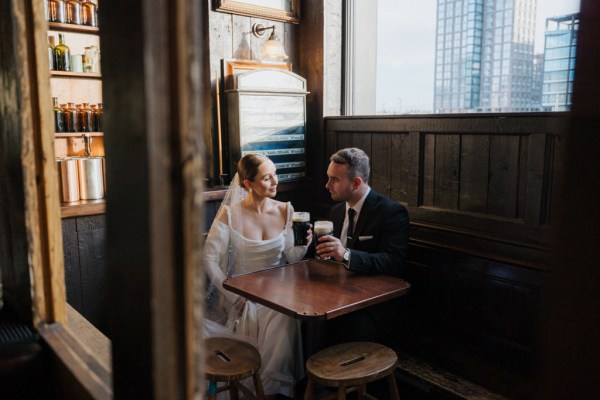 bride and groom sit in pub setting and cheers with pint of Guinness