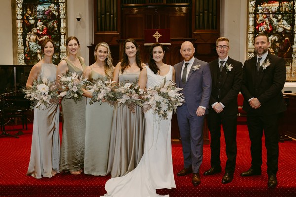 bride and groom surrounded by groomsmen and bridesmaids standing on red carpet