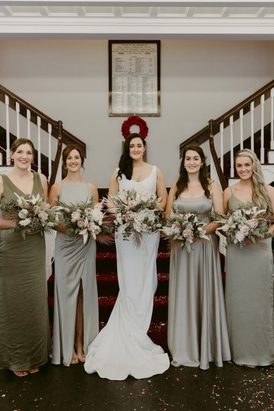 bride and bridesmaids stand beside staircase interior setting