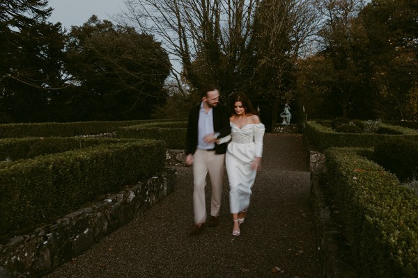 bride and groom walk hand in hand down the pathway to garden