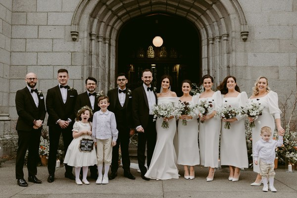 bride groom little boy and girl bridesmaids and groomsmen all stand outside church entrance