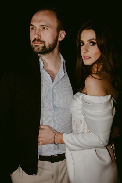 bride faces camera and places hand on grooms waist while groom looks the other way