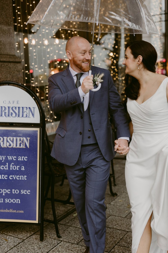 bride and groom walk in the rain holding up umbrella