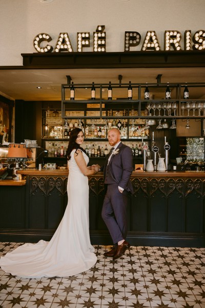 bride and groom stand at bar Cafe Paris sign