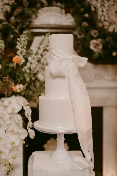 white wedding cake surrounded by candles lit white flowers/roses white ribbon