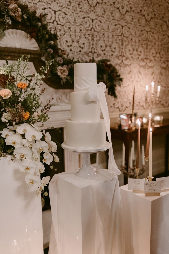 white wedding cake surrounded by candles lit white flowers/roses