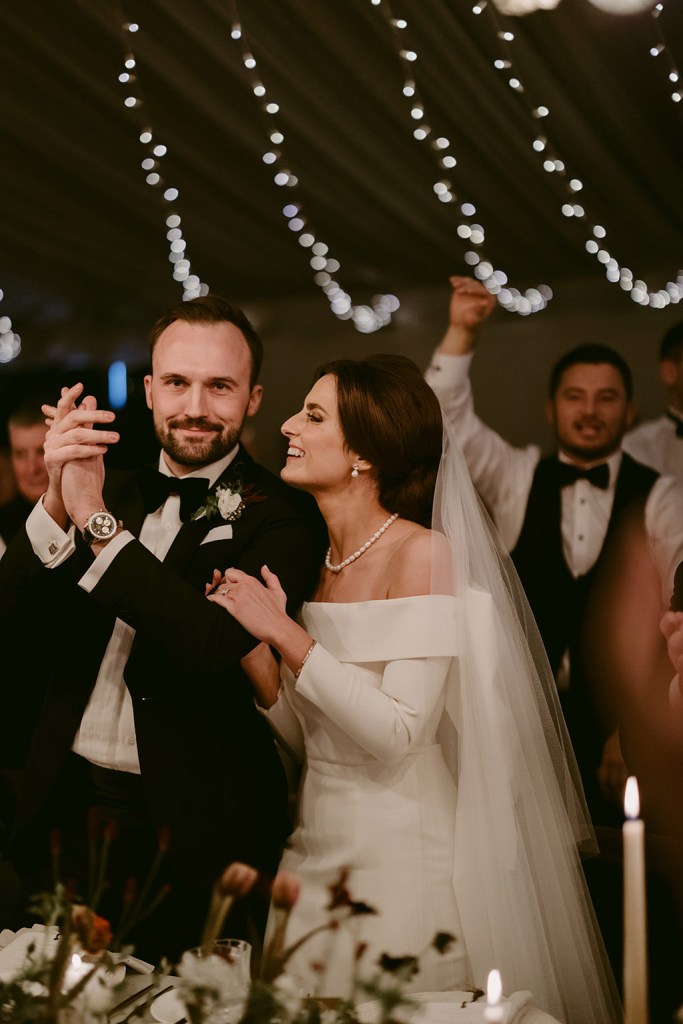 bride and groom clap along with guests in background marquee tent