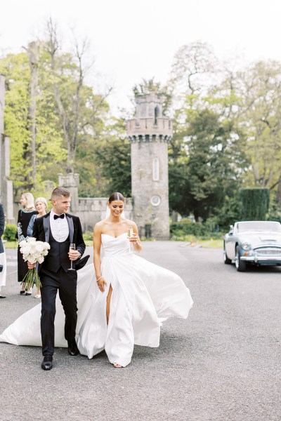 bride and groom outside walking hand in hand he holds her white roses flowers bouquet