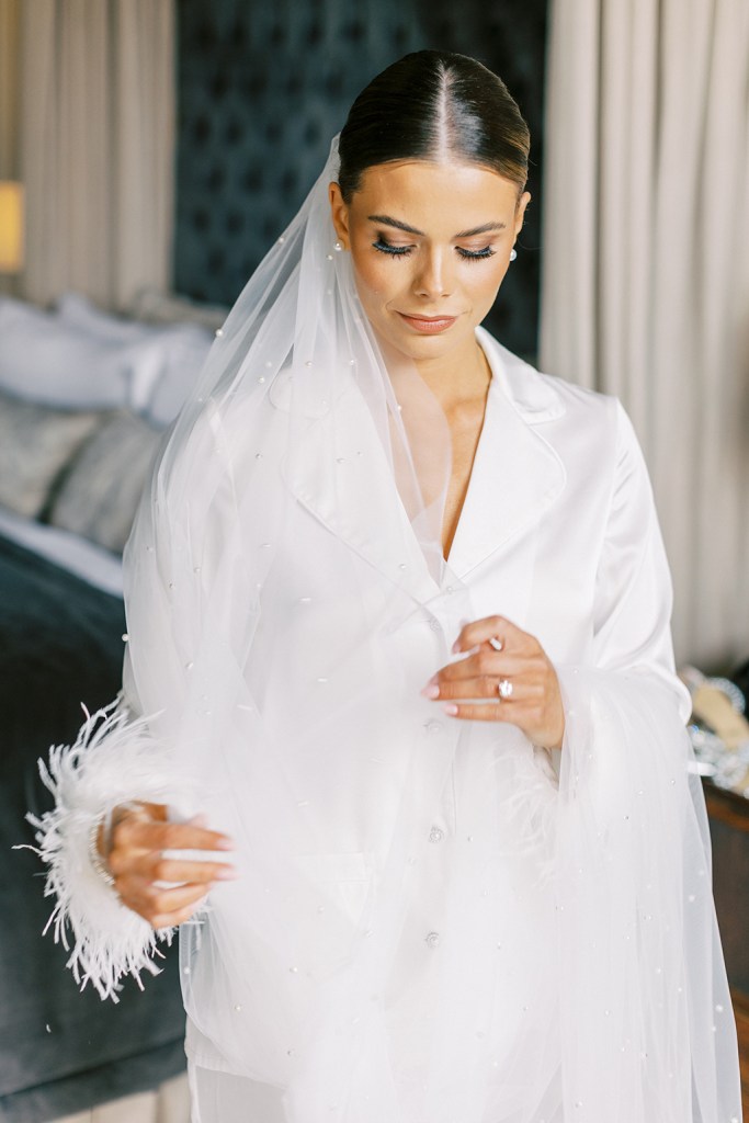 bride looks down holding veil wearing white loungewear