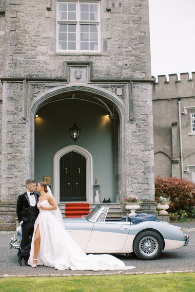 bride and groom face each other looking at each other holding glass of champagne prosecco wide shot outside wedding beside wedding car