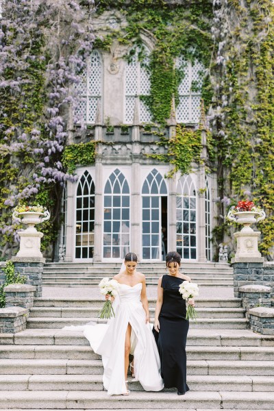 bride holding white roses bouquet with sister/bridesmaid wearing black dress exterior wedding venue