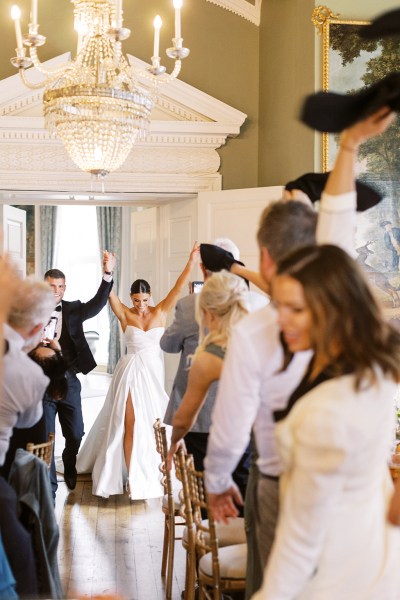 bride and groom throw hands arms in the air surrounded by clapping happy guests