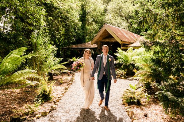 bride and groom walk the pathway to garden smiling holding hands