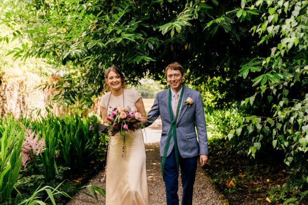 bride and groom walk the pathway to garden smiling