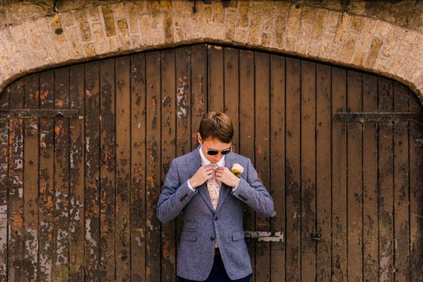 groom looks down in front of wooden gate fixes tie