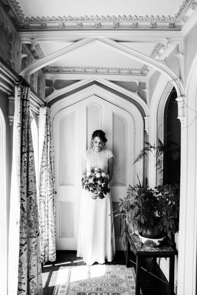 bride standing underneath archway to wedding venue black and white