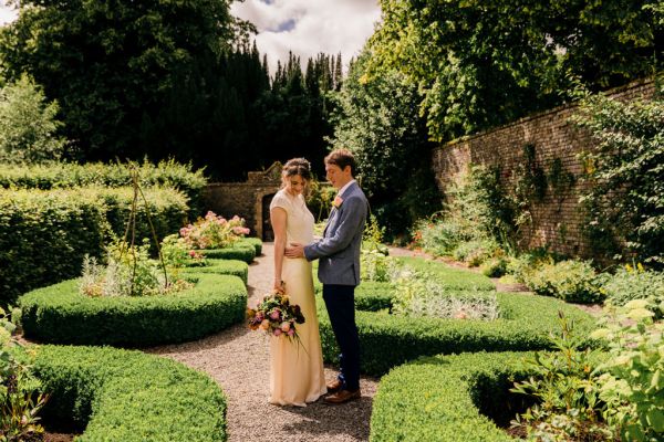 bride and groom in the gardens she holds bouquet hugging